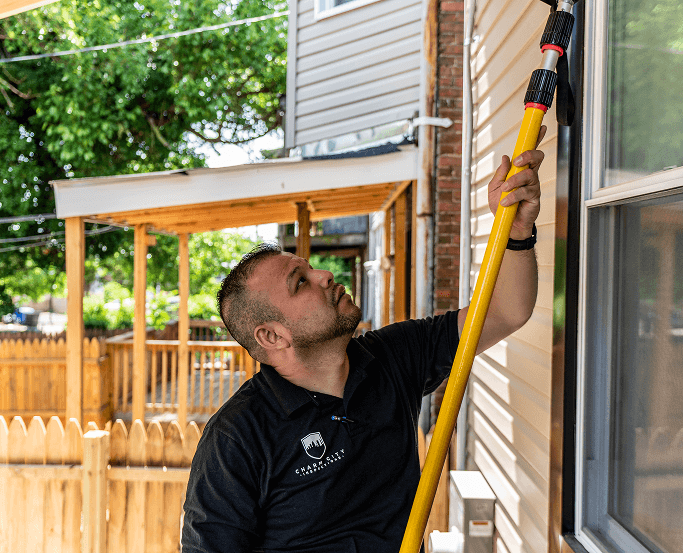 An inspector using a yellow extension pole to inspect the exterior of a house
