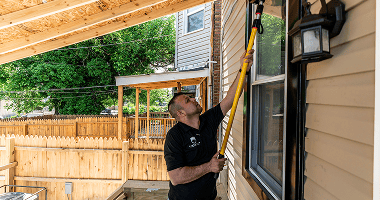 An inspector using a yellow extension pole to check the outside of a house